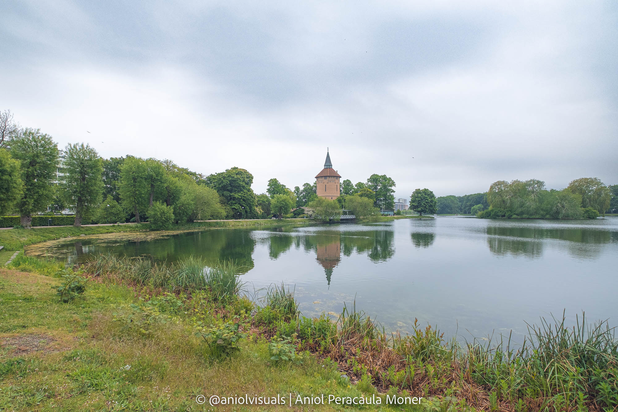 A cloudy day in a green park in Malmö with a big lake and an old tower construction reflected in it